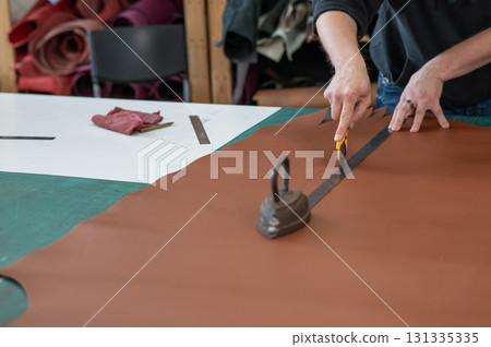 Leatherworker measuring and cutting leather in workshop. Leatherworker measuring and cutting leather in workshop. 131335335