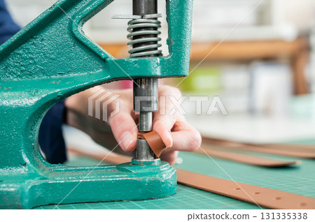 A woman attaches accessories to a leather belt. Leatherworker's workshop.  131335338