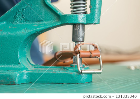 A woman attaches accessories to a leather belt. Leatherworker's workshop.  131335340