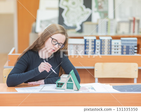 Caucasian young woman making a model of a building. Student of the construction university. Caucasian young woman making a model of a building. Student of the construction university. 131335350