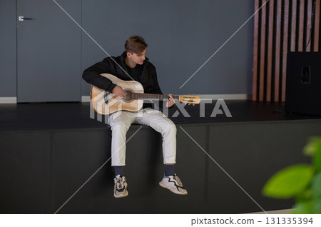 Caucasian man playing guitar while sitting on stage.  131335394