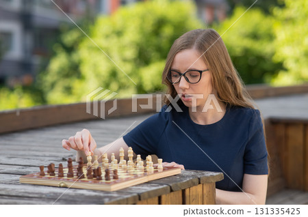 Caucasian woman playing chess outdoors. Caucasian woman playing chess outdoors. 131335425