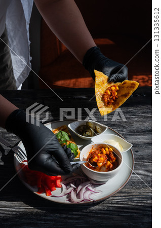 A chef wearing black gloves prepares fajitas.  131335612