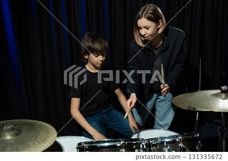 Young caucasian woman teaches a boy to play the drums in the studio on a black background. Music school student Young caucasian woman teaches a boy to play the drums in the studio on a black background. Music school student 131335672
