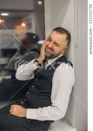 Thoughtful Caucasian man sitting on windowsill in office. Thoughtful Caucasian man sitting on windowsill in office. 131335738