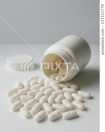 White tablets spilling from an open plastic bottle on a clean white background. Perfect for 131335779