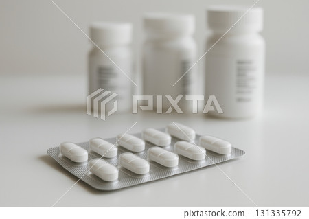 White capsules in a silver blister pack placed on a clean surface with unfocused white pill bottles White capsules in a silver blister pack placed on a clean surface with unfocused white pill bottles 131335792