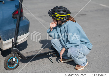 A distressed woman examines the damage after a collision between an electric scooter and a car. A distressed woman examines the damage after a collision between an electric scooter and a car. 131335804