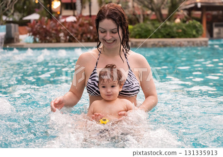Caucasian woman holds her son while swimming in a pool on vacation. Mom teaches little boy to swim.  131335913