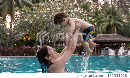 Caucasian woman holds son while swimming in pool on vacation.  131335918