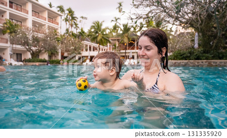 Caucasian woman holds her son while swimming in a pool on vacation. Mom teaches little boy to swim.  131335920