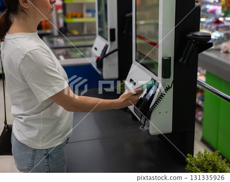 A woman pays using her smartphone at a self-checkout.  131335926