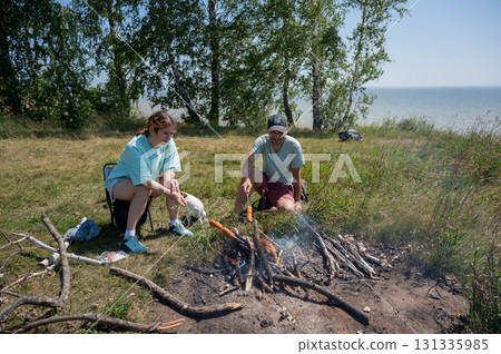 Caucasian couple roasting sausages over a fire.  131335985