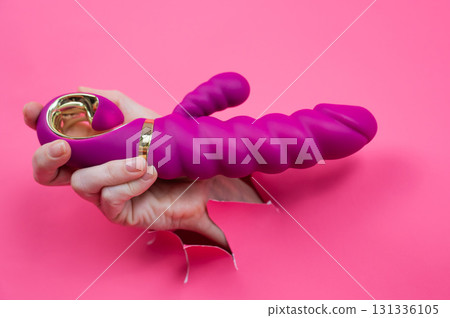 Female hand sticking out with pink sex toy from pink paper background. 131336105