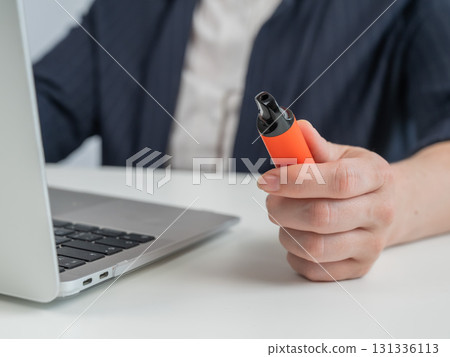 Faceless businesswoman smokes disposable vape and works on laptop.  131336113