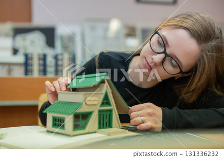 Caucasian young woman making a model of a building. Student of the construction university. Caucasian young woman making a model of a building. Student of the construction university. 131336232