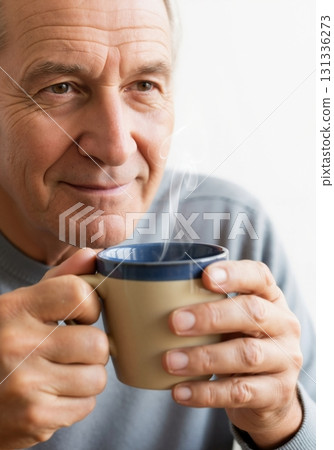 Senior man smiling while holding a mug of hot coffee or tea. Close-up portrait of a happy older person relaxing. Retirement lifestyle concept Senior man smiling while holding a mug of hot coffee or tea. Close-up portrait of a happy older person relaxing. Retirement lifestyle concept 131336273