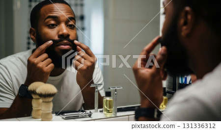 Black man styling his mustache in a bathroom mirror. Men's grooming and self-care routine. Facial hair maintenance concept 131336312