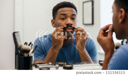 Black man grooming his mustache in the mirror. Morning self-care routine with styling products. Masculine hygiene and personal care concept 131336313