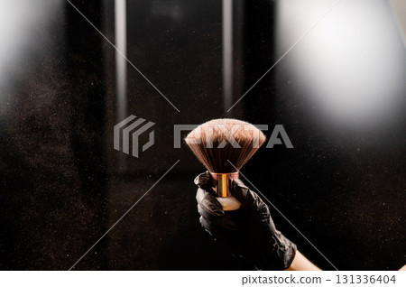 A woman shakes a large powder brush with clouds of dust on a black background. Treatment after instant tanning A woman shakes a large powder brush with clouds of dust on a black background. Treatment after instant tanning 131336404