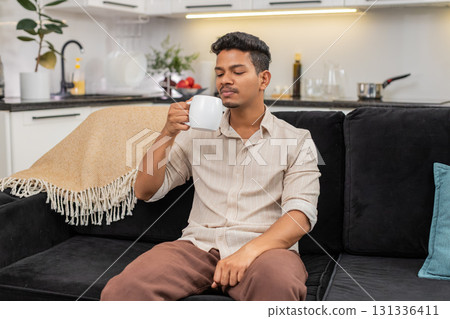 Indian man drinks hot tea holds mug takes calm sip relax mind enjoys morning before work start fresh Indian man drinks hot tea holds mug takes calm sip relax mind enjoys morning before work start fresh 131336411
