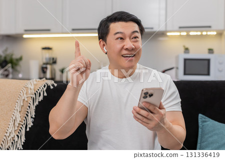 Asian man studies online course on smartphone in headphones finds solution shows ok sign sets goal Asian man studies online course on smartphone in headphones finds solution shows ok sign sets goal 131336419