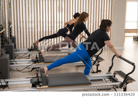 Three Asian women doing Pilates on a reformer. Three Asian women doing Pilates on a reformer. 131336420