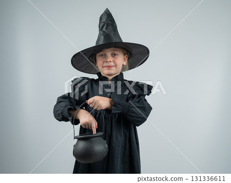 Portrait of a little Caucasian girl in a witch costume holding a cauldron on a white background.  131336611