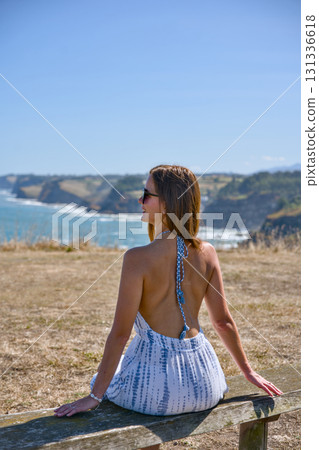 Young woman sitting on bench looking at ocean coast 131336618