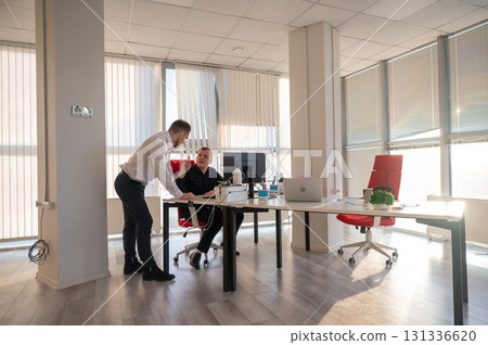 Caucasian man standing at colleague's desk discussing work. Caucasian man standing at colleague's desk discussing work. 131336620
