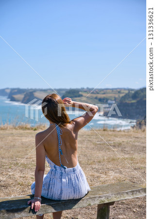 Young woman sitting on bench looking at ocean coast Young woman sitting on bench looking at ocean coast 131336621