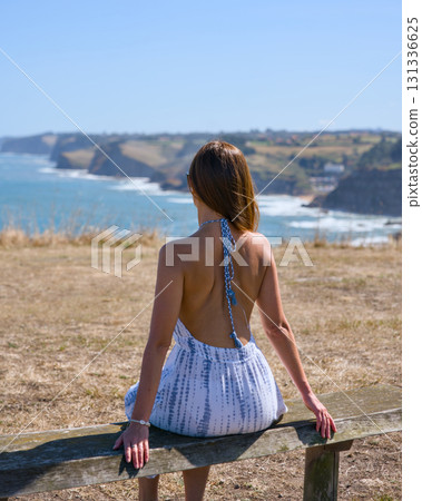 Young woman sitting on bench facing ocean horizon 131336625
