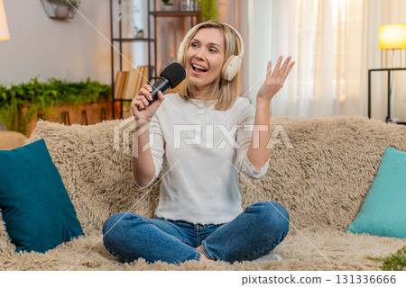 Adult woman singing with headphones and microphone at home dancing joyfully feeling like a superstar 131336666