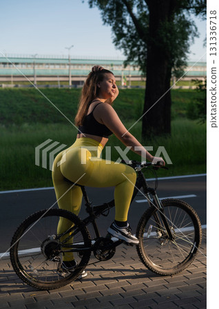 A Caucasian woman in yellow leggings and a crop top rides a bicycle in tights in the park. A Caucasian woman in yellow leggings and a crop top rides a bicycle in tights in the park. 131336718