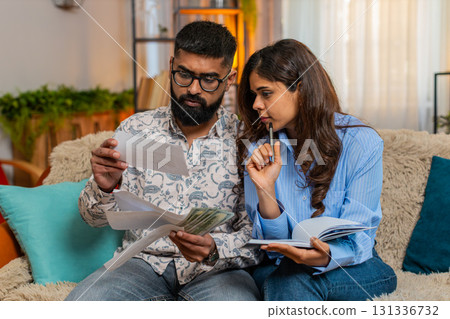 Indian family couple man woman calculating bills money at home, making notes reacting frustration 131336732