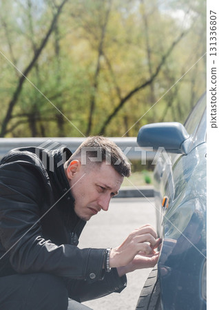 A Caucasian man inspects damage to his car. A Caucasian man inspects damage to his car. 131336807
