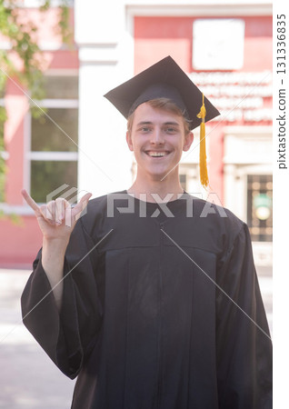 Caucasian young man in graduation gown communicating using sign language.  131336835