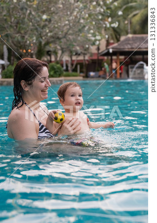 Caucasian woman holds son while swimming in pool on vacation. Caucasian woman holds son while swimming in pool on vacation. 131336843