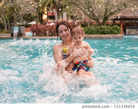 Caucasian woman holds her son while swimming in a pool on vacation. Mom teaches little boy to swim. Caucasian woman holds her son while swimming in a pool on vacation. Mom teaches little boy to swim. 131336858