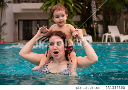Caucasian woman holds her son while swimming in a pool on vacation. Mom teaches little boy to swim. Caucasian woman holds her son while swimming in a pool on vacation. Mom teaches little boy to swim. 131336860