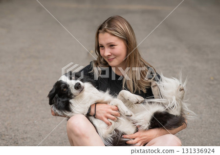 Young caucasian woman sitting on asphalt and hugging border collie dog.  131336924