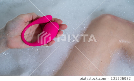 A woman lies in a bubble bath and holds a curved pink vibrator. 131336982