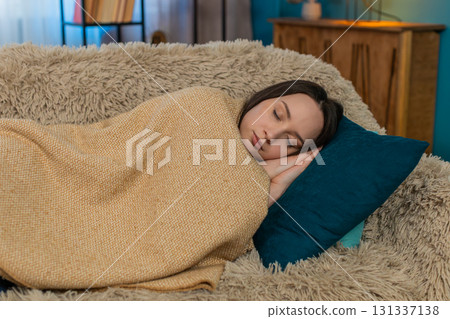 Woman falling asleep tired after exhausting day wrapped in blanket laying head on pillow on sofa 131337138