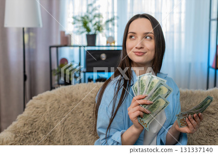 Young woman happily counting pile of cash dollar bills on sofa celebrating wealth successful finance Young woman happily counting pile of cash dollar bills on sofa celebrating wealth successful finance 131337140