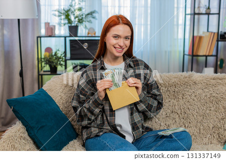 Woman sitting on sofa counting cash dollars putting part into envelope looking happy and satisfied Woman sitting on sofa counting cash dollars putting part into envelope looking happy and satisfied 131337149
