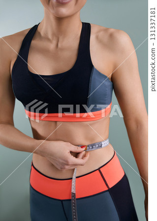 Weight loss, slim body, healthy lifestyle concept. Fit fitness girl measuring her waistline with measure tape. 131337181