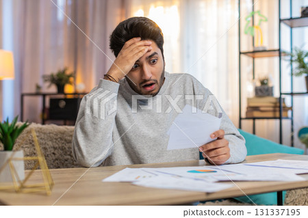 Young Indian man frustrated with bills and expenses while reviewing documents at home on table 131337195