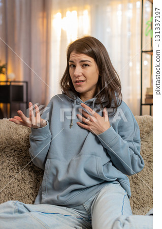 Confused Caucasian woman on sofa raising eyebrows feeling embarrassed about ambiguous question Confused Caucasian woman on sofa raising eyebrows feeling embarrassed about ambiguous question 131337197