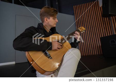 Caucasian man playing guitar while sitting on stage. Caucasian man playing guitar while sitting on stage. 131337198