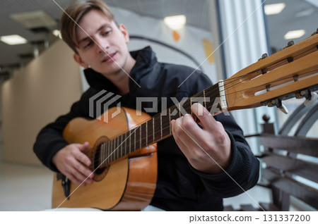 Caucasian man playing guitar while sitting on a bench.  131337200